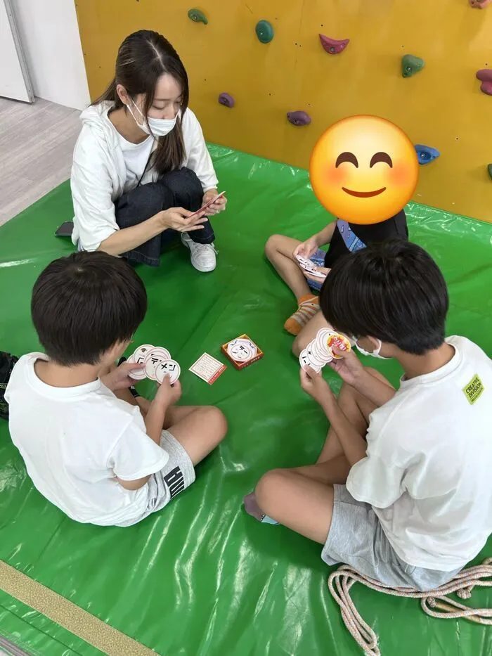 マットの上で輪になってカードゲーム「音速飯店」を楽しむ子どもたちと職員