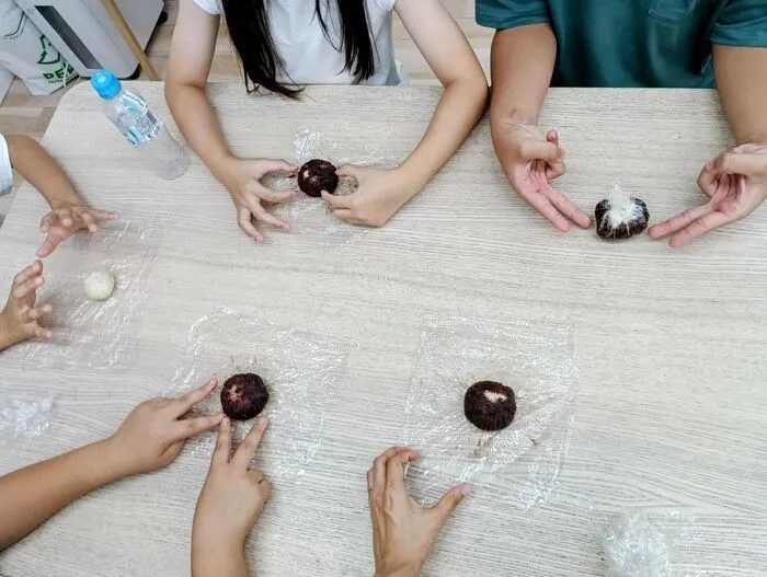 ラップの上でもち米とあんこを丸めておはぎを作る子どもたちの手元