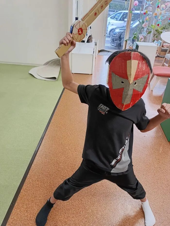 手作りのヒーローのお面と剣で、ポーズを決めてなりきり遊びをする子ども