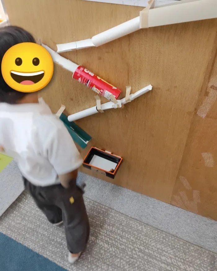 空き箱や芯をつないで壁に作ったボールのコースを組み立てる子ども(顔は隠しています)