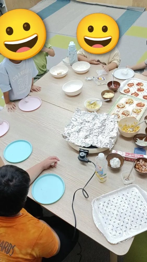 餃子の皮やトッピングの具材が並ぶテーブルを囲むピザパーティーの様子