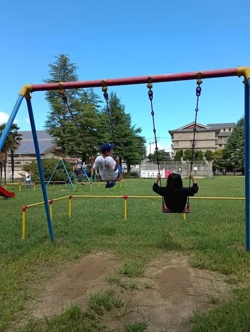 青空の下の公園でブランコに乗る子どもたち
